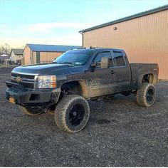 a black pickup truck parked in front of a building with mud all over it's tires