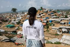 a woman standing on top of a dirt hill next to a village filled with houses