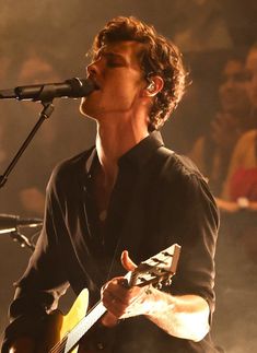 a man holding a guitar while singing into a microphone