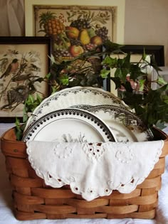 a basket filled with plates sitting on top of a white tablecloth covered floor next to framed pictures