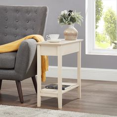 a gray chair with a yellow blanket on it next to a white end table and potted plant