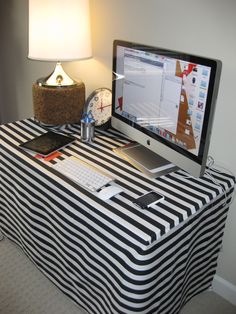 a computer monitor sitting on top of a black and white table cloth covered desk next to a lamp