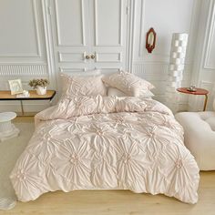 a white bed with pink comforter and pillows in a room next to a chair