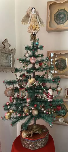 a small christmas tree with ornaments on it and an angel statue in the top right corner