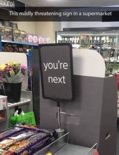 a sign that says you're next in front of some snacks and flowers at a store