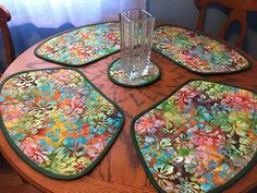 four placemats on top of a wooden table with a vase and glass in the middle