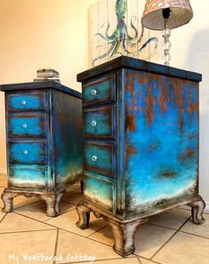 two blue dressers sitting on top of a tiled floor next to a lamp and painting