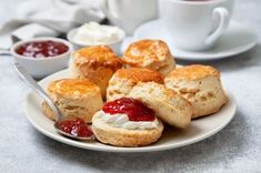 scones with jam and cream on a white plate next to two cups of tea