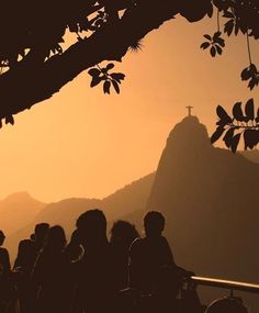 silhouettes of people sitting under a tree in front of a mountain with a cross on it