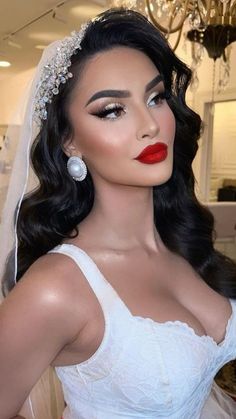 a woman wearing a wedding dress and veil with red lipstick on her lips is standing in front of a chandelier