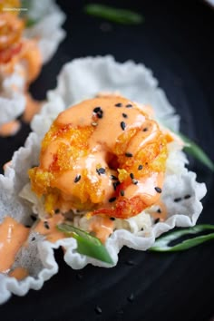 a black plate topped with sushi covered in sauce