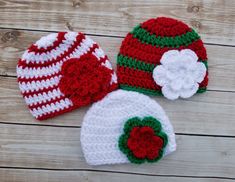 three crocheted hats are laying on a wooden surface, one is red and the other is white