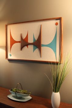 a painting hanging on the wall above a table with a bowl and plant in it