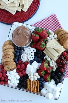 a platter filled with crackers, strawberries, raspberries, marshmallows and other snacks