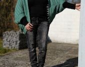 a woman in black shirt and jeans standing next to a white pillar with her hand out