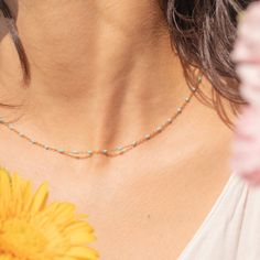 a close up of a woman wearing a necklace with beads and flowers in the background