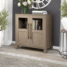 a clock on the wall above a cabinet with flowers and books in front of it