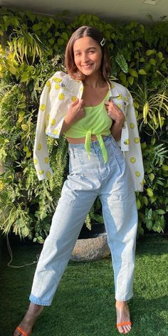 a woman standing in front of a green wall wearing jeans and a yellow top with polka dots on it