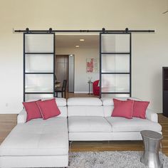 a living room with a white sectional couch and red pillows on the rug in front of an open sliding glass door