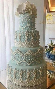 a three tiered blue wedding cake with white flowers on the top and pearls around the edges