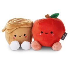 two small stuffed animals sitting next to each other on a white surface, one has an apple and the other has a piece of bread in it's mouth