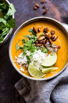 a bowl filled with carrot soup and garnished with cilantro, lime wedges and nuts