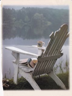 a wooden chair sitting on top of a grass covered field next to a body of water