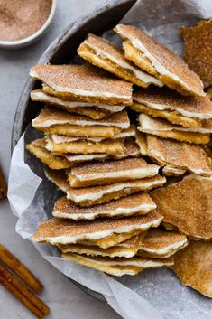 a plate full of pancakes with cinnamon sticks next to it and dipping sauce on the side