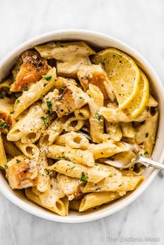 a white bowl filled with pasta and lemon wedges on top of a marble table