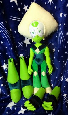 a green alien stuffed animal sitting on top of a blue blanket with stars around it