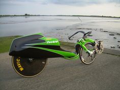 a green and black motorcycle parked on the side of a road next to some water