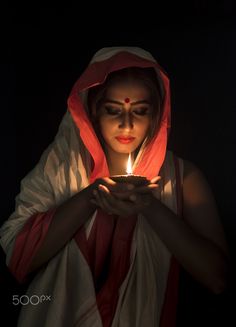 a woman holding a lit candle in her hands while wearing a red and white robe