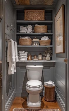 a white toilet sitting inside of a bathroom next to a wooden shelf filled with towels