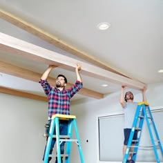 two men standing on ladders holding up beams