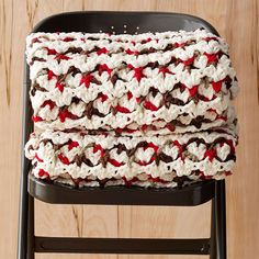 two crocheted blankets sitting on top of a black chair next to a wooden wall