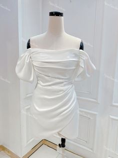 a white dress on a mannequin stand in front of a wall and door