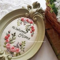 an embroidered welcome home sign with pink flowers in a basket next to it on a table