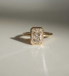 a yellow gold ring with a square shaped diamond in the center, sitting on a white surface