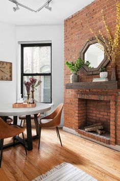 Corner dining space created in NYC apartment. Cement dining table is paired with leather dining chairs, highly durable and comfortable. An original brick fireplace sits as the backdrop with a dark wood floating mantle. We used organic accessories to style the space: rattan mirror, succulents, vase with tall branches, and a variety of glasses on the dining table. Floating Mantle Fireplace, Speakeasy Decor Bar, Fireplace Dark, Light Wood Dining Table, Floating Mantle, Speakeasy Decor, Brick Living Room, Red Brick Fireplaces, Decorative Fireplace