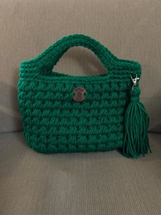 a green crocheted purse sitting on top of a couch next to a pillow