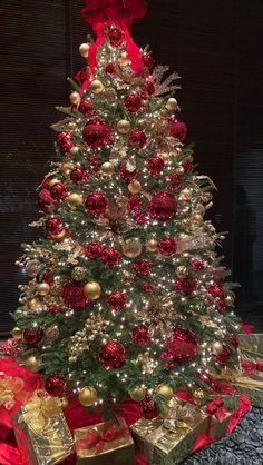 a christmas tree with red and gold ornaments on it's top, surrounded by presents