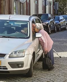 an older woman leaning out the window of a car with her hand on the door handle