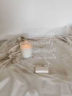 a white candle sitting on top of a bed next to a sign that says your wings are ready