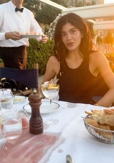 a woman sitting at a table with food in front of her and another man standing behind her