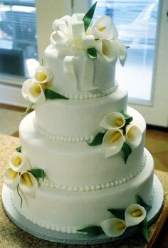 a three tiered cake with white and yellow flowers on the top, sitting on a counter