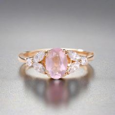 an oval shaped pink sapphire and diamond ring with three pears on the band, set in yellow gold