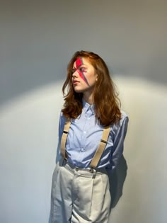 a woman wearing suspenders and a blue shirt is standing in front of a white wall