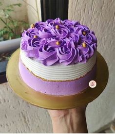 a hand holding a cake with purple flowers on it