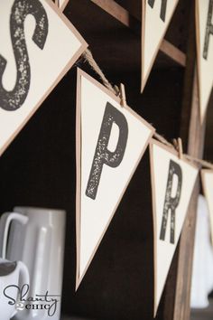 a wooden sign with letters hanging from it's sides on a shelf next to coffee mugs