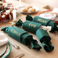 two green napkins with name on them sitting on a table next to plates and silverware